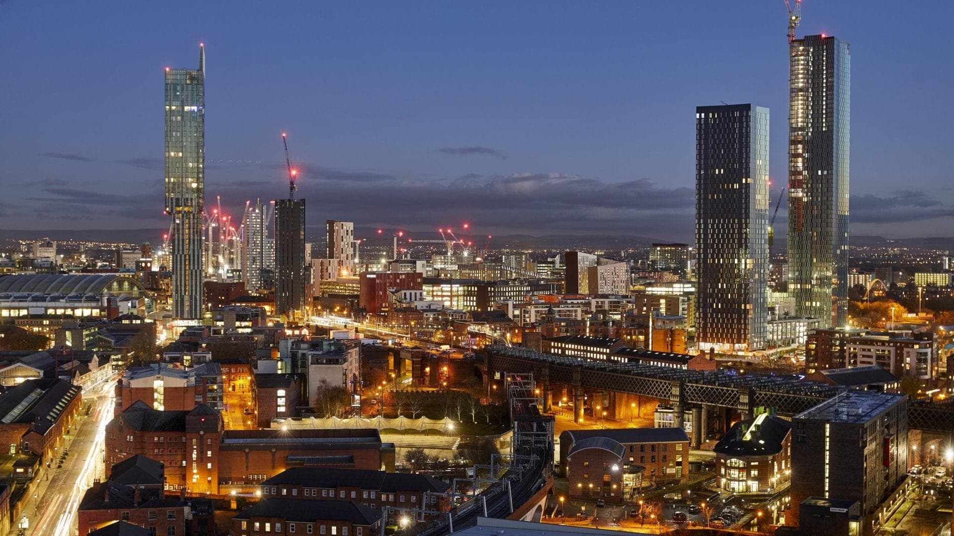 The Manchester skyline at dusk, with the Deansgate Square towers and the lit railway viaduct